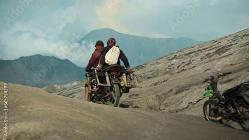 Two Indonesian people on a motorcycle ride through a volcanic desert photo