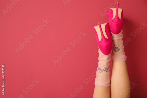 Tattooed female legs in heels on pink background, back view