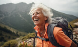 An elderly woman climbs to the top of a mountain with a backpack and smiles happily