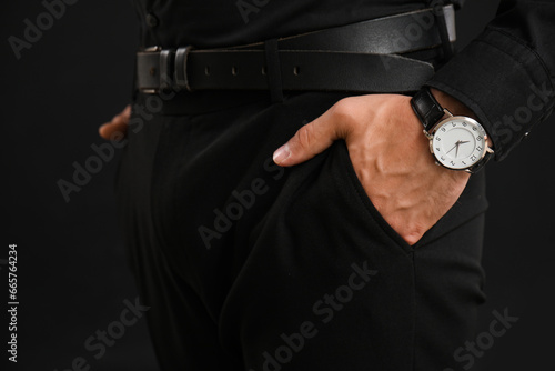Elegant young man with wristwatch on black background, closeup