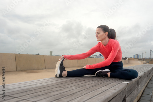 Sporty woman doing leg stretching exercises, outside. Outdoor workout.