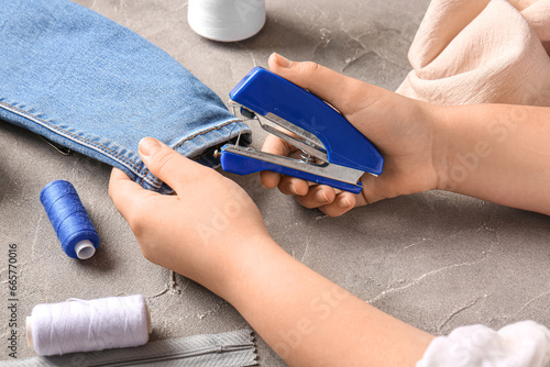 Foto Female hands with different supplies sewing jeans on grunge grey background