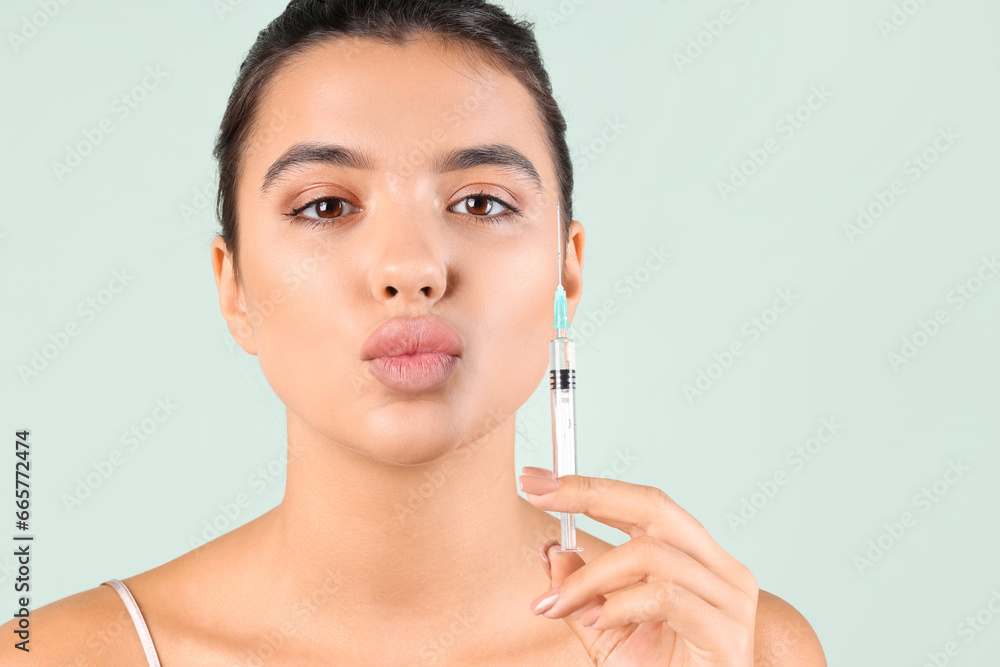 Young woman with beautiful lips and syringe blowing kiss on green background, closeup Young woman with beautiful lips and syringe blowing kiss on green background, closeup