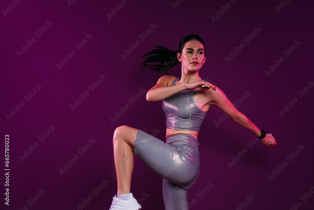 Young slim woman in silver sportrswear warming up her body over magenta backdrop