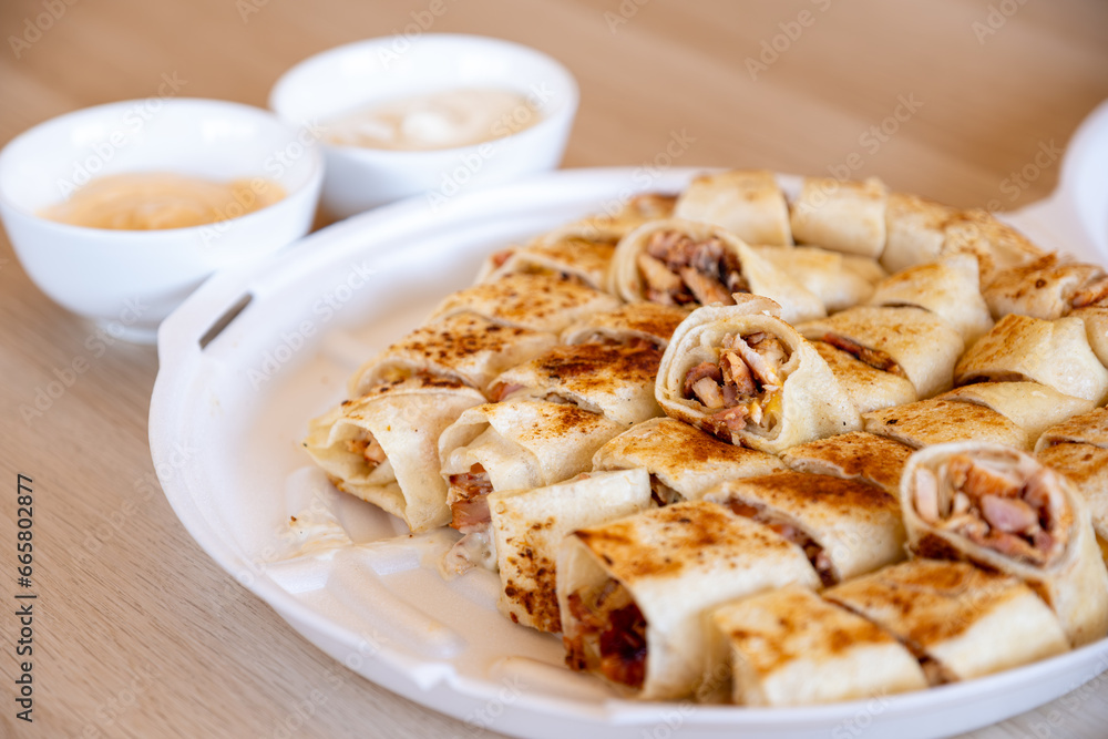 Pieces of shawarma on wooden table with dips and arranged on white plate