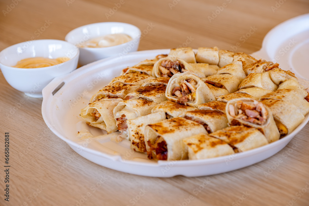 Pieces of shawarma on wooden table with dips and arranged on white plate