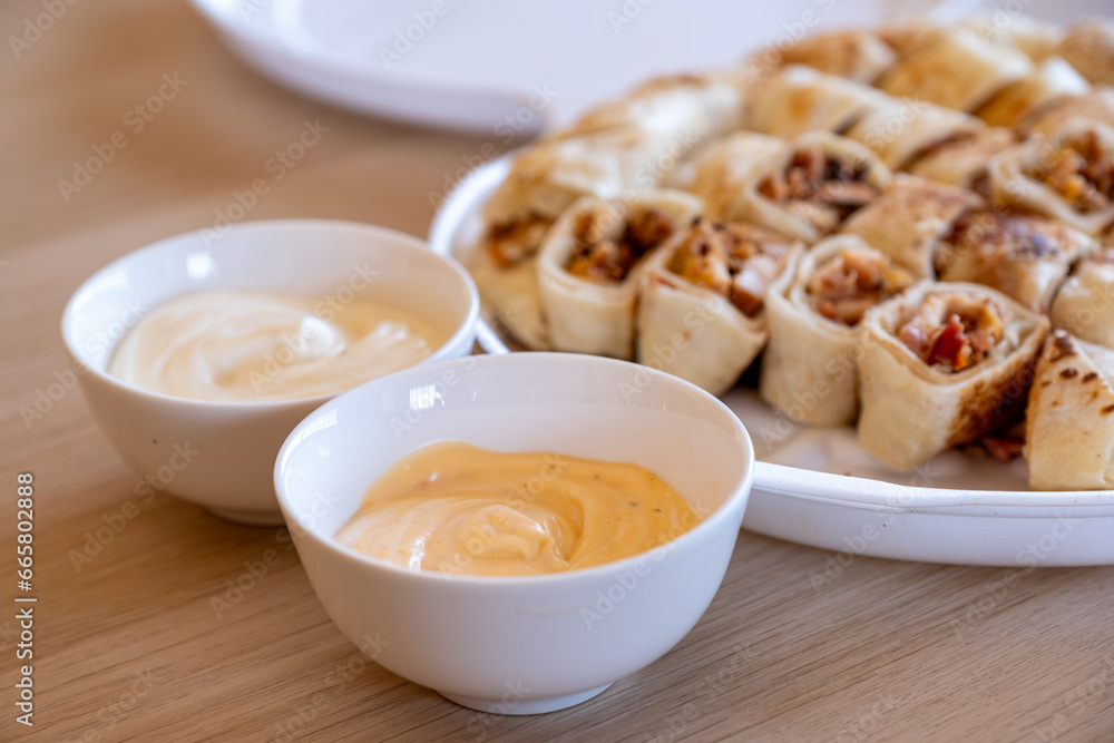 Pieces of shawarma on wooden table with dips and arranged on white plate