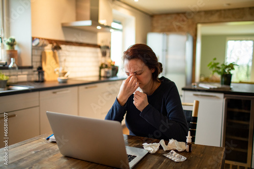 Sick woman with a cold blowing nose in a tissue at home photo