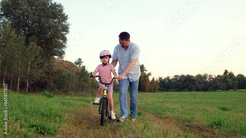 Careful father teaches little girl to ride bicycle in wild summer park