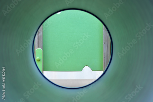 Photograph from inside a cylindrical tunnel of a playground to the outside of the tunnel. Selective focus on the front panel of the exterior of the cylindrical tunnel. Space to copy