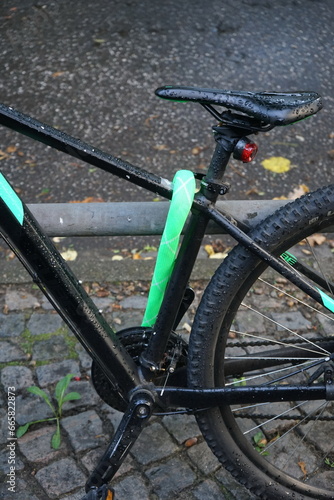 Modernes Mountainbike in Schwarz mit grün ummanteltem Fahrradschloss bei Regenwetter mit Regentropfen auf dem Sattel im Stadtteil Harvestehude an der Alster in der Hansestadt Hamburg photo