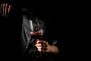 woman hands pouring red wine into a glass from a bottle on black background