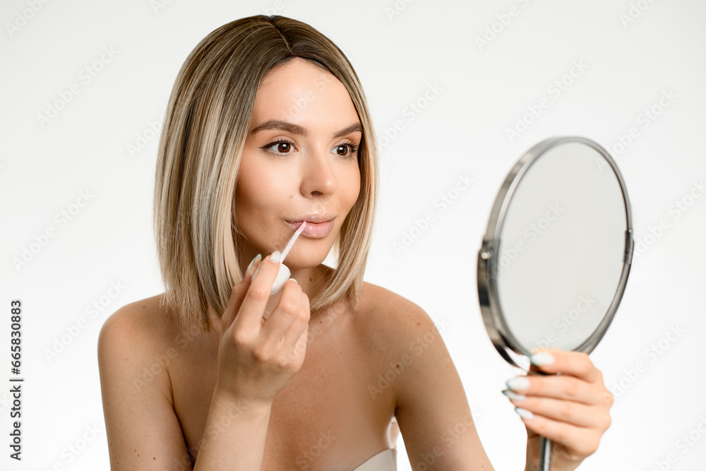 Pretty blonde woman looks in the mirror and applies lips gloss Pretty blonde woman looks in the mirror and applies lips gloss
