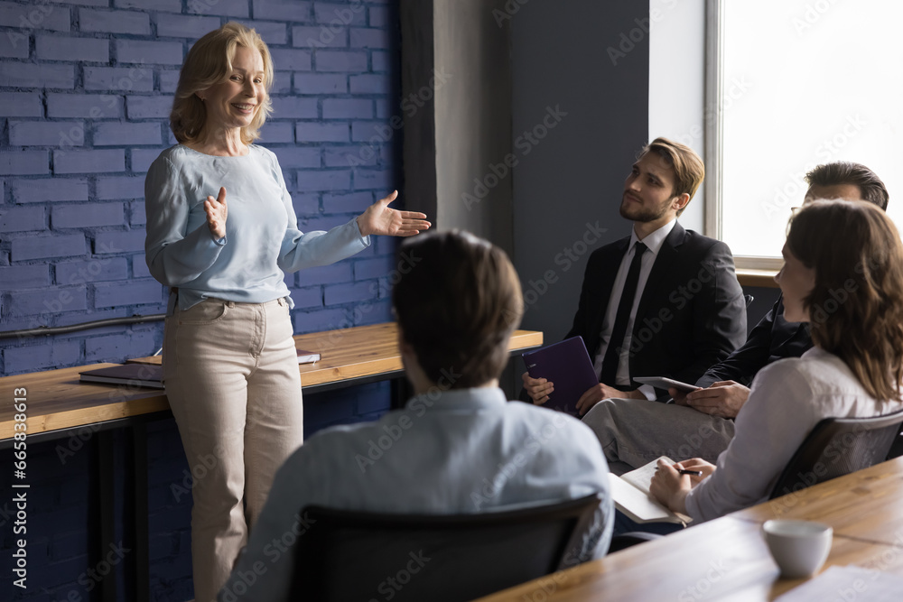 Cheerful corporate leader woman give seminar to young employee, discuss work on project. Confident mentor instructs team of businesspeople, explain new project strategy. Briefing, mentoring, teamwork Cheerful corporate leader woman give seminar to young employee, discuss work on project. Confident mentor instructs team of businesspeople, explain new project strategy. Briefing, mentoring, teamwork