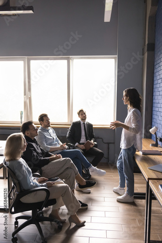Serious attractive young business coach woman speak before office team explaining task, discuss work project. Successful mentor conduct seminar in boardroom for company managers. Leadership, mentoring