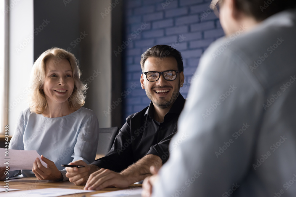Φωτογραφία Smiling different ages employees looking at colleague at team meeting, listen new project idea sitting at desk in office room