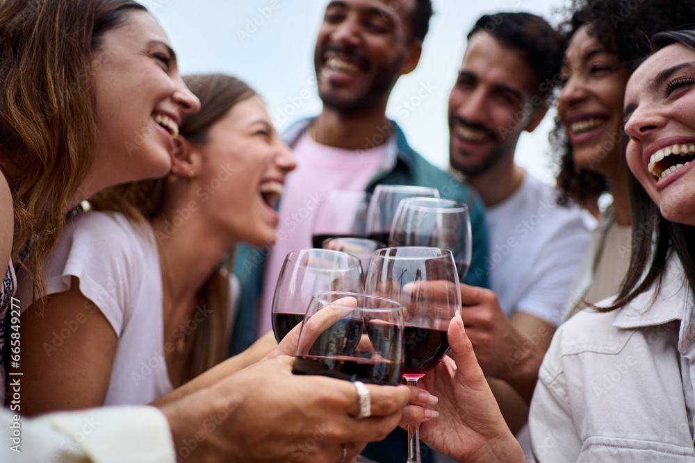 Group multiracial laughing friends toasting glasses red wine and celebrating party outdoors. Young people together cheers on open air. Boys and girls enjoying free time on summer weekend vacation. Group multiracial laughing friends toasting glasses red wine and celebrating party outdoors. Young people together cheers on open air. Boys and girls enjoying free time on summer weekend vacation.