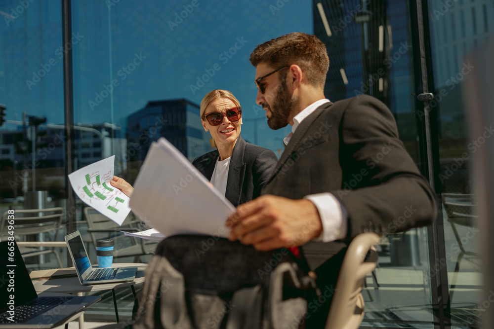 Business colleagues working with documents sitting outside of office on cafe terrace Business colleagues working with documents sitting outside of office on cafe terrace