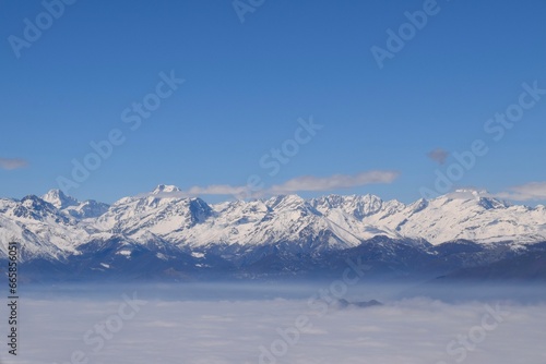 Beautiful aerial view of alpine snowcapped mountain range peaking through heavy clouds. Mountain peaks of Italian alps from above. The impressive winter view is taken from an airplane window.