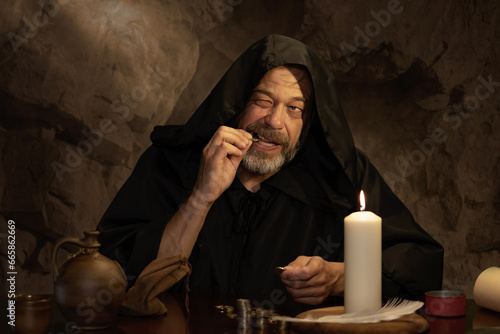 Fototapeta A monk authenticates money by candlelight in a dark stone room, stacks of coins