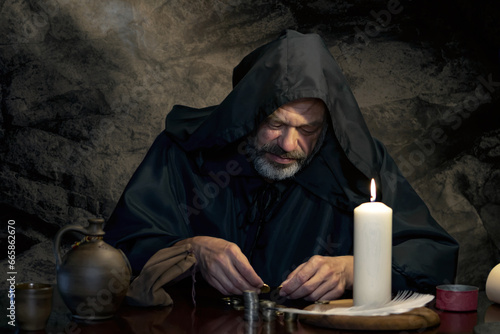 A monk in a robe counts money or coins by candlelight in a dark stone room. A tax collector in medieval times, a church treasurer. photo