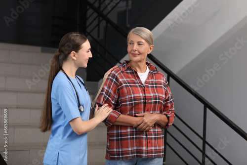 Young healthcare worker assisting senior woman on stairs indoors