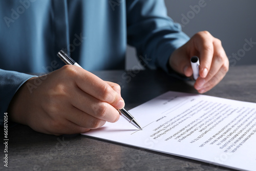 Woman signing document with pen at grey table, closeup