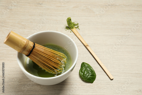 Cup of fresh green matcha tea with bamboo whisk and spoon on wooden table, space for text