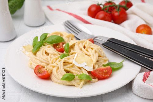 Delicious pasta with brie cheese, tomatoes, basil and cutlery on white tiled table, closeup