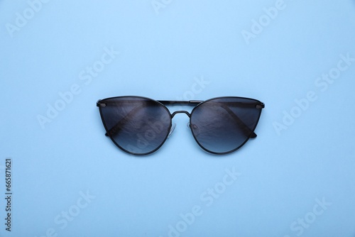 Stylish sunglasses on light blue background, top view