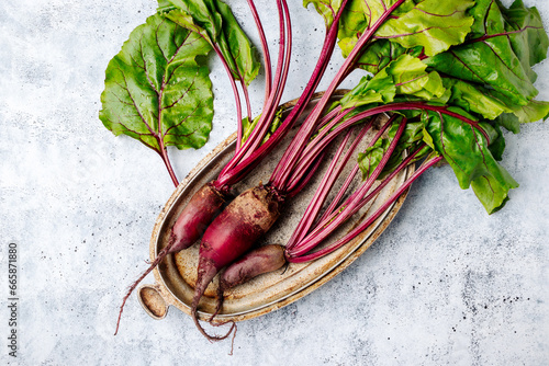 Fresh raw beets with leaves on a rustic metal dish on a gray background photo