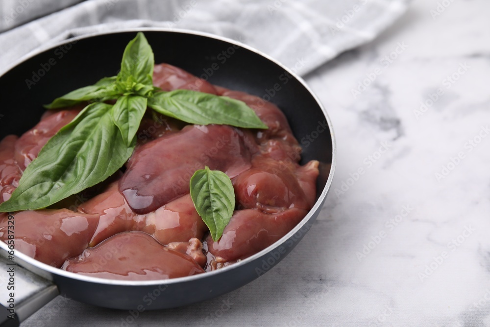 Raw chicken liver with basil in frying pan on white marble table, closeup