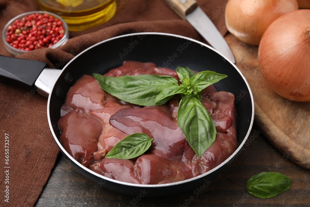 Raw chicken liver with basil in frying pan on wooden table Raw chicken liver with basil in frying pan on wooden table