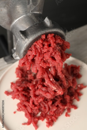 Mincing beef with metal meat grinder on light table, closeup