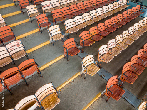 Old faded orange and yellow painted wooden seats at a abandoned a stadium grandstand.
