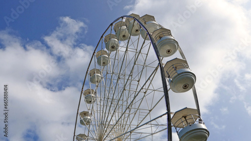 A photo of a large white Ferris Panoramic wheel spinning on a sunny day with blue sky