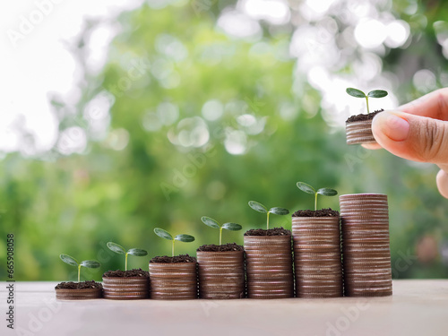 Close up hand putting coins with plants growing up on stack of coins. The concept of saving money, Financial, Investment and Business growing. photo