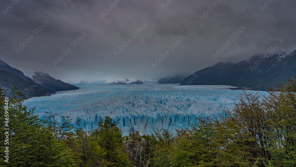 The beautiful Perito Moreno Glacier stretches between the mountains to the horizon. An endless mass of blue ice with sharp peaks, cracks, crevices. Cloudy, foggy. Argentina. El Calafate
