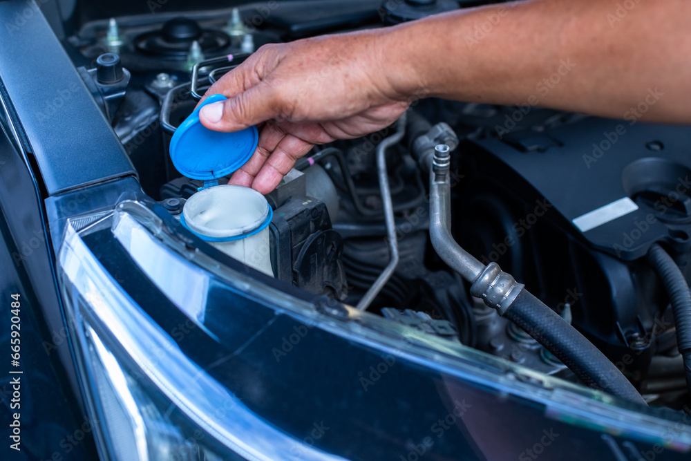 Mechanic fill fresh water into windscreen or in water tank wiper on car engine room.
