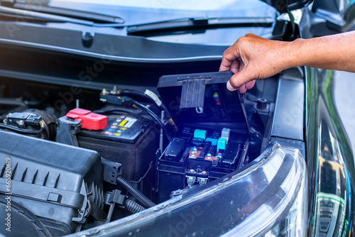 A mechanic is opening the cover of a car's electrical system control box.