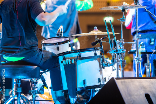 Selective focus to drum set and drummer with blurry music band in concert.