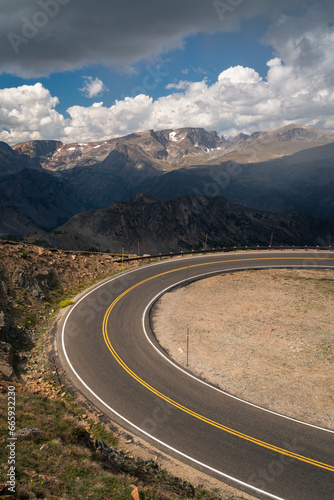 Curving alpine road with distant mountains and clouds