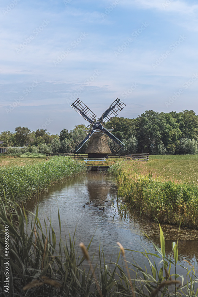 wooden windmill stands by the water in a field in the Netherlands
