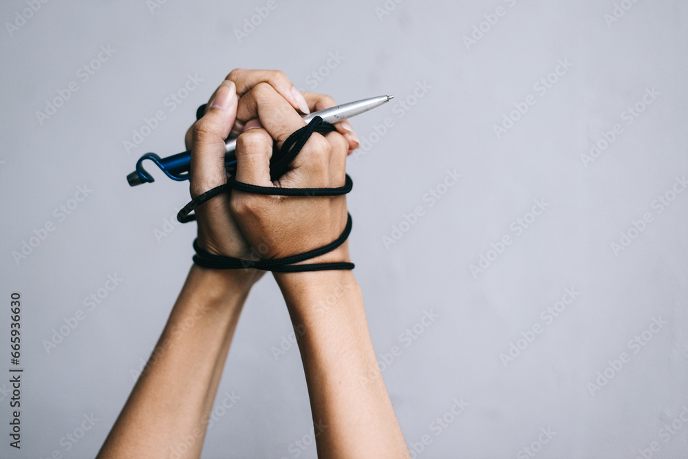 Hands with silver pen tied with rope, depicting the idea of freedom of the press or freedom of expression and international human rights day concept. Hands with silver pen tied with rope, depicting the idea of freedom of the press or freedom of expression and international human rights day concept.