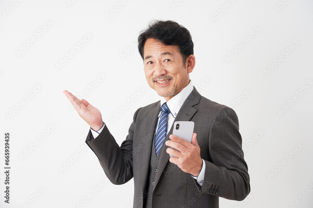 スマートフォンを持って左側を手のひらで指す中年のビジネスマン 白背景 スマートフォンを持って左側を手のひらで指す中年のビジネスマン 白背景