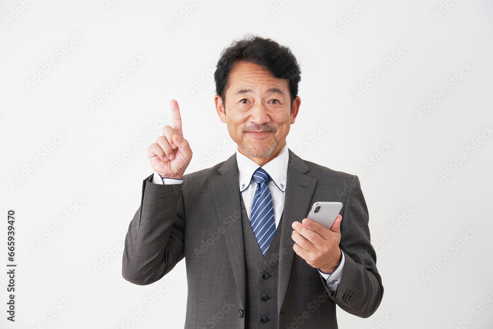 スマートフォンを持って上方向を指差す中年のビジネスマン　白背景