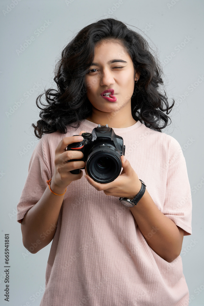 A girl playfully forms a heart shape with her lips while cradling a camera, capturing moments of love and joy.