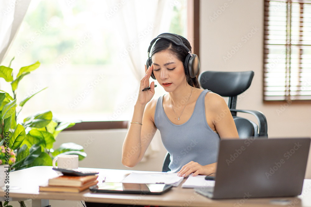Freelancer Young business asian woman wear wireless headphone and working at home with laptop and papers on desk Freelancer Young business asian woman wear wireless headphone and working at home with laptop and papers on desk