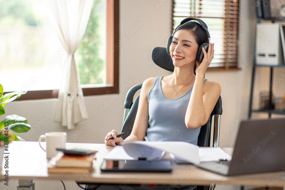 Obraz premium Freelancer Young business asian woman wear wireless headphone and working at home with laptop and papers on desk