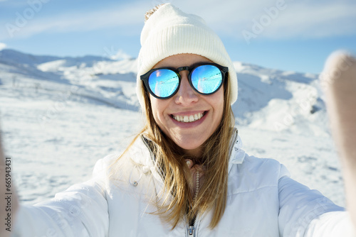 Cheerful woman in sunglasses taking selfie in snowy mountains